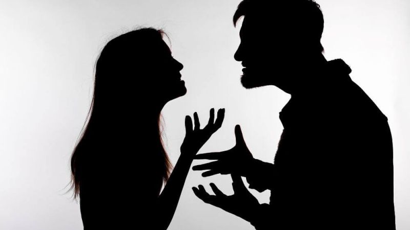 A man and woman are silhouetted against a light background, engaged in a heated argument with expressive hand gestures and intense facial expressions, suggesting conflict and emotional tension.