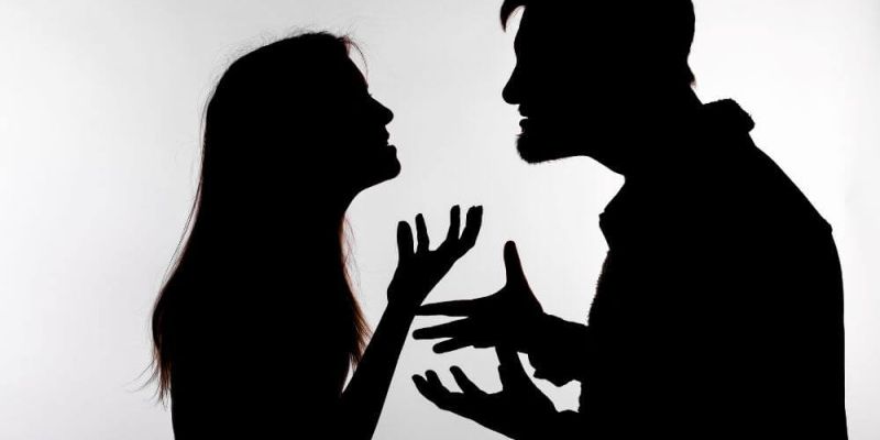 A man and woman are silhouetted against a light background, engaged in a heated argument with expressive hand gestures and intense facial expressions, suggesting conflict and emotional tension.
