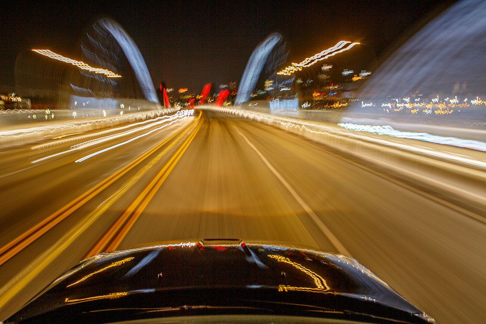 Motion blur of a car driving fast at night on a brightly lit bridge.