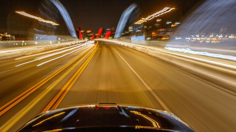 Motion blur of a car driving fast at night on a brightly lit bridge.