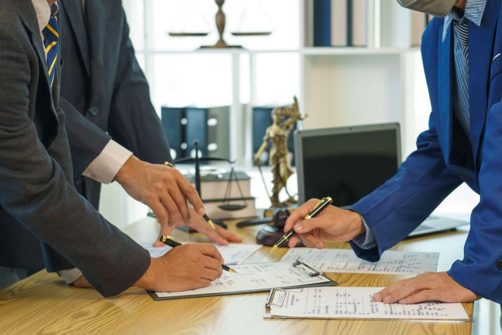 Lawyers discussing documents at a desk with legal scales and laptop in background.