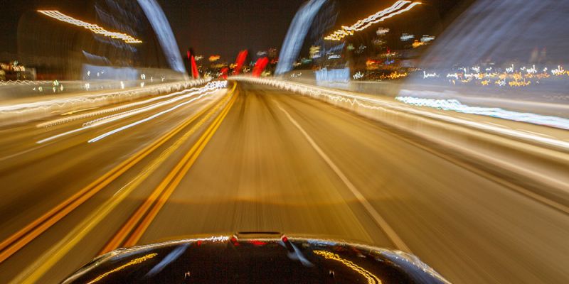Motion blur of a car driving fast at night on a brightly lit bridge.