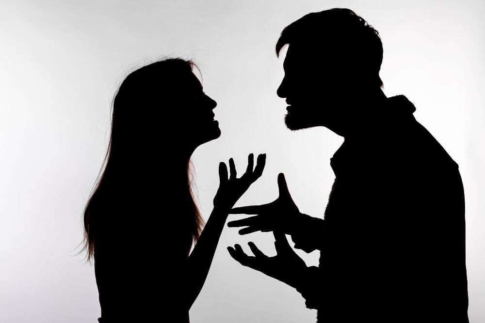 A man and woman are silhouetted against a light background, engaged in a heated argument with expressive hand gestures and intense facial expressions, suggesting conflict and emotional tension.