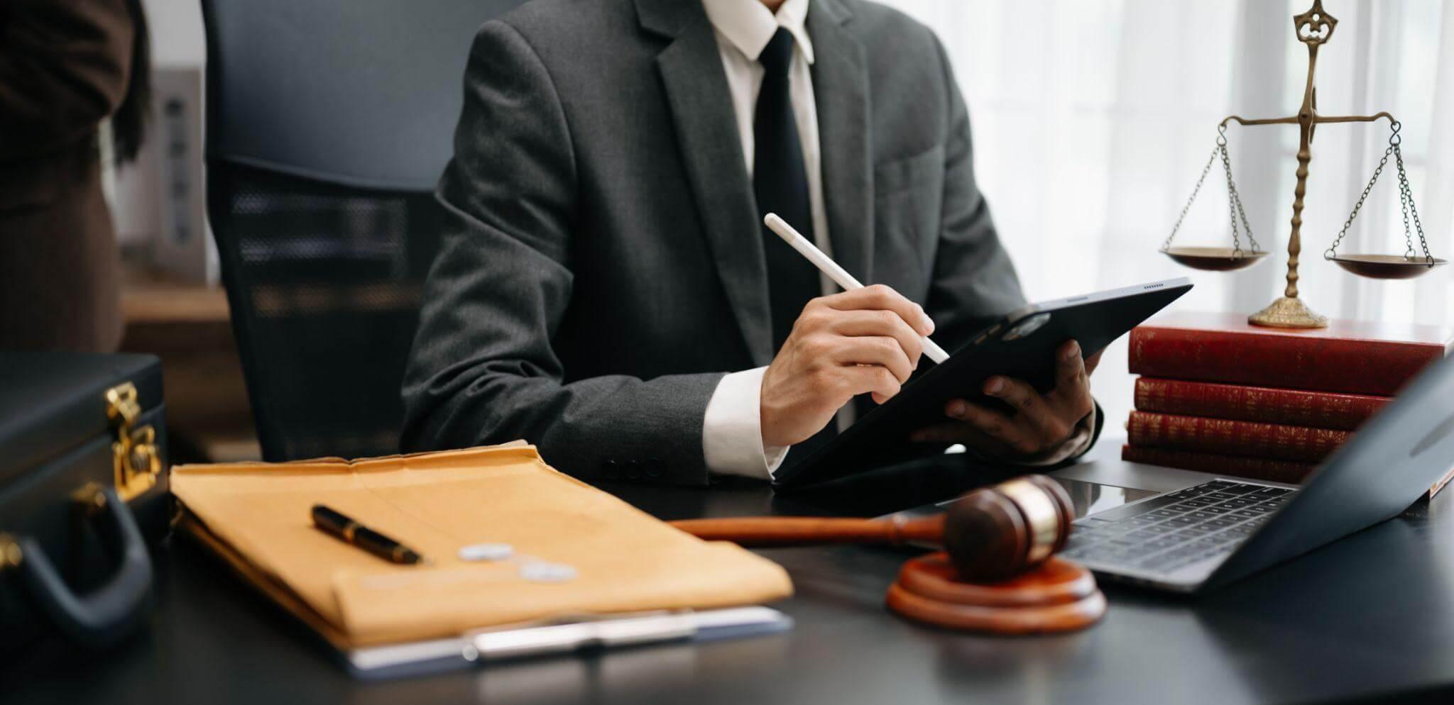 a man sitting at a desk in front of a laptop and writing on a tablet